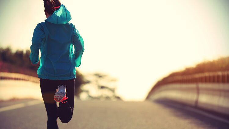 Ambitionierte Läuferin beim Lauftraining auf einer Straße im Sonnenaufgang