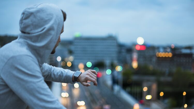 Athlete checking his smartwatch above the city at dawn