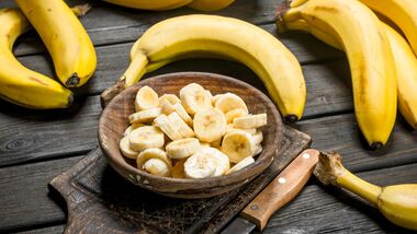 Bananas and banana pieces in a wooden plate on a cutting Board with a knife.