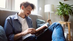 Ein Mann sitzt auf dem Sofa und liest in einem Buch.