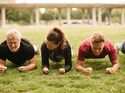 Eine Gruppe trainiert auf dem Rasen die Plank. Training der Rumpfmuskulatur mit dem Unterarmstütz.
