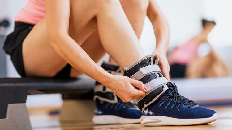 Eine Sportlerin befestigt Gewichtsmanschetten an ihren Fußgelenken.