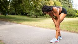 Eine junge Läuferin fasst an ihr vor Muskelkater schmerzendes Bein.