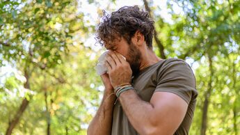 Fließschnupfen: Ein Mann putzt sich in einer sommerlichen Umgebung die laufende Nase