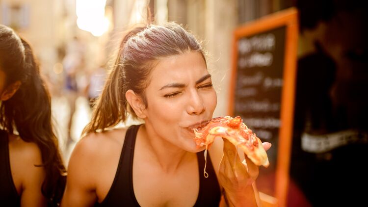 Lebensmittel-No-Gos vorm Laufen: Eine Sportlerin isst ein Stück fettige Pizza.