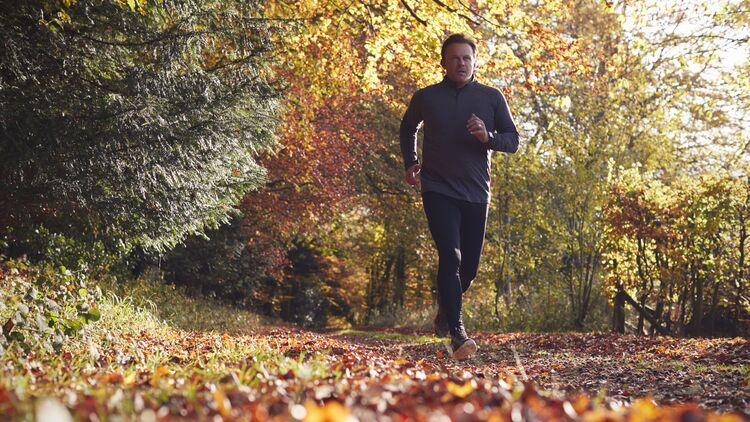 Low Angle View Of Mature Man Running Through Autumn Woodland