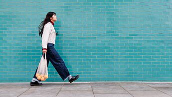 Mehr Bewegung im Alltag: Eine junge Frau kommt zu Fuß vom Einkaufen zurück und trägt ein Netz mit Orangen.