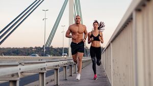 Sixpack durch Joggen: Ein Läufer und eine Läuferin mit sehr athletischem Körperbau joggen über eine Brücke.