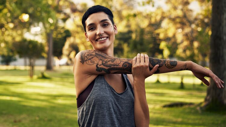 Sport mit Tattoo: Junge Frau mit Tätowierung dehnt sich nach dem Joggen.
