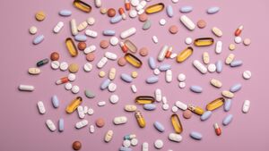 Top view of spoon with various pills and tablets on the pink background