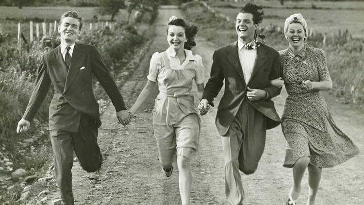 Two couples holding hands, running on footpath, (B&W)